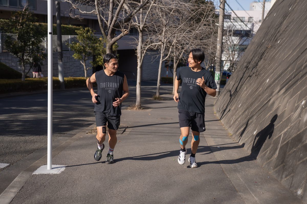 TIGERRUNS RUNNING CLUB のウェアを着て並んで走る2人の後ろ姿